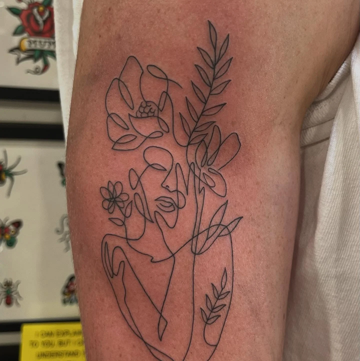 Tattoo of a line art portrait of a woman with floral and leaf elements on the arm.
