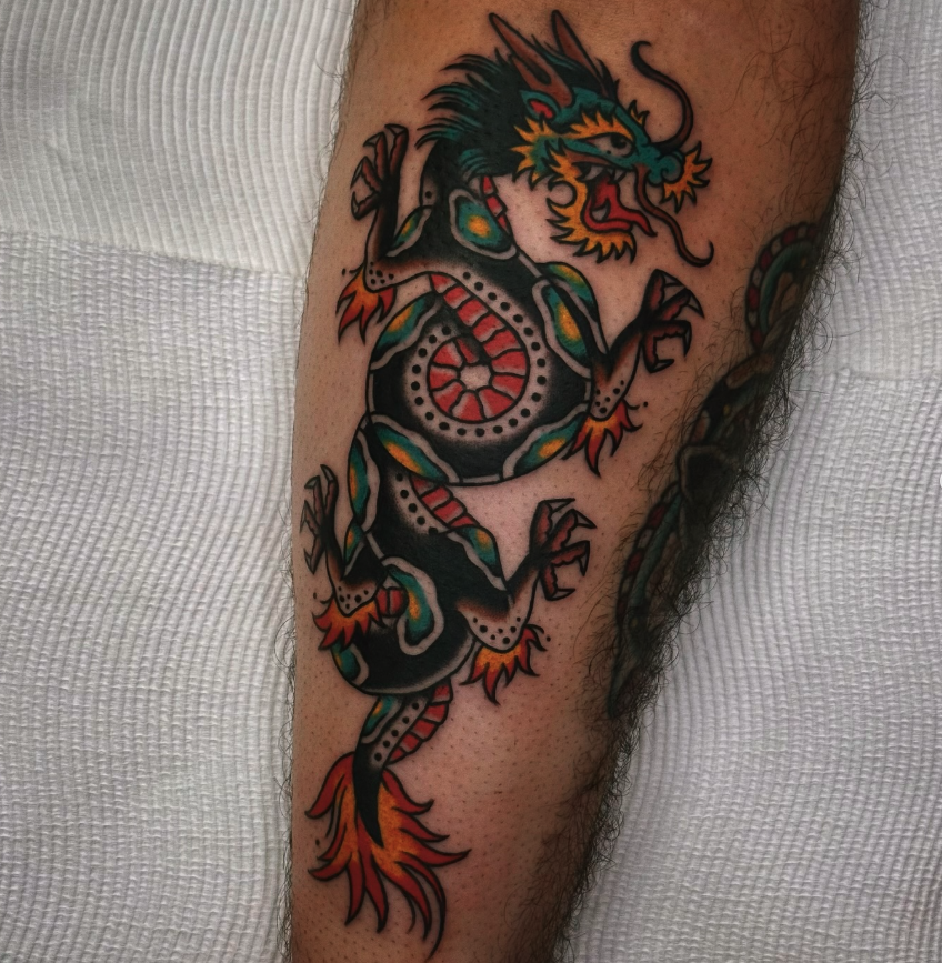 Colorful traditional Asian dragon tattoo on person's forearm with black, orange, green, and yellow hues.