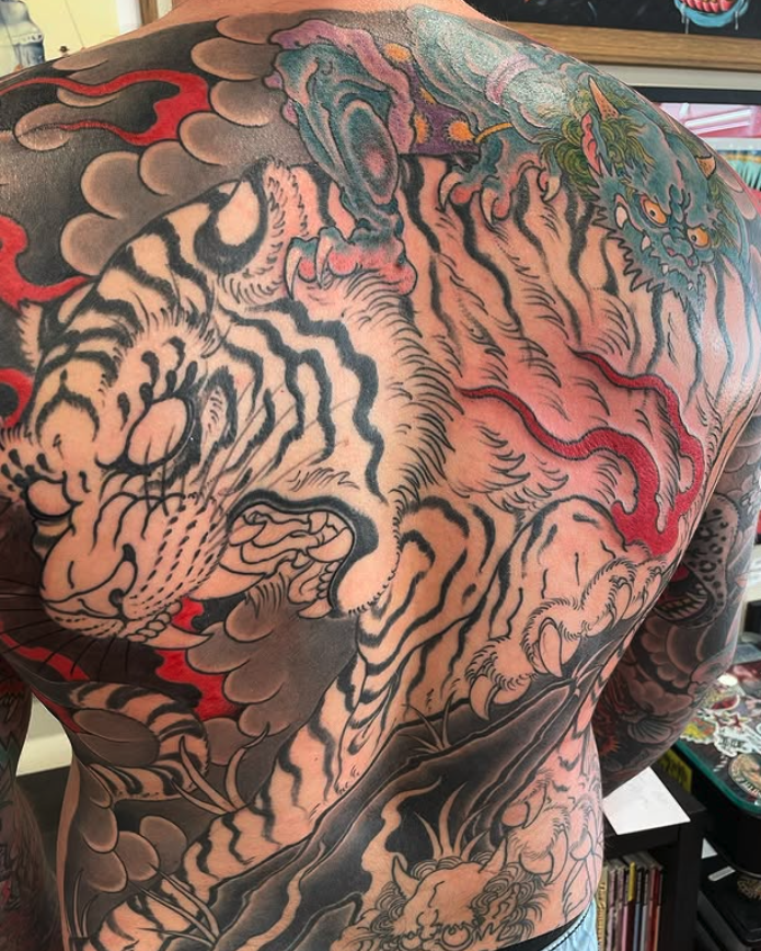Close-up of a colorful tattoo depicting a tiger and a dragon on a person's back and shoulder.