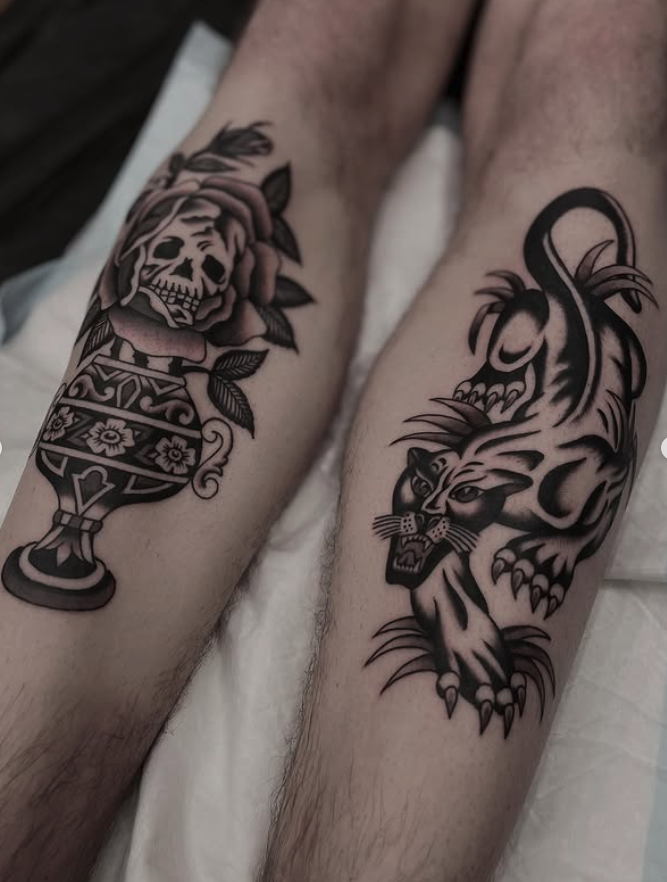 Tattoo of a skull with a rose and leaves on one thigh, and a fierce tiger illustration on the other thigh.