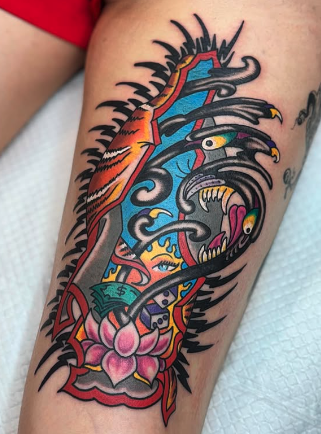 Colorful tattoo featuring a shield, a venomous snake, a lotus flower, a dollar bill, and a woman's face, all in bold, traditional style on a person's arm.