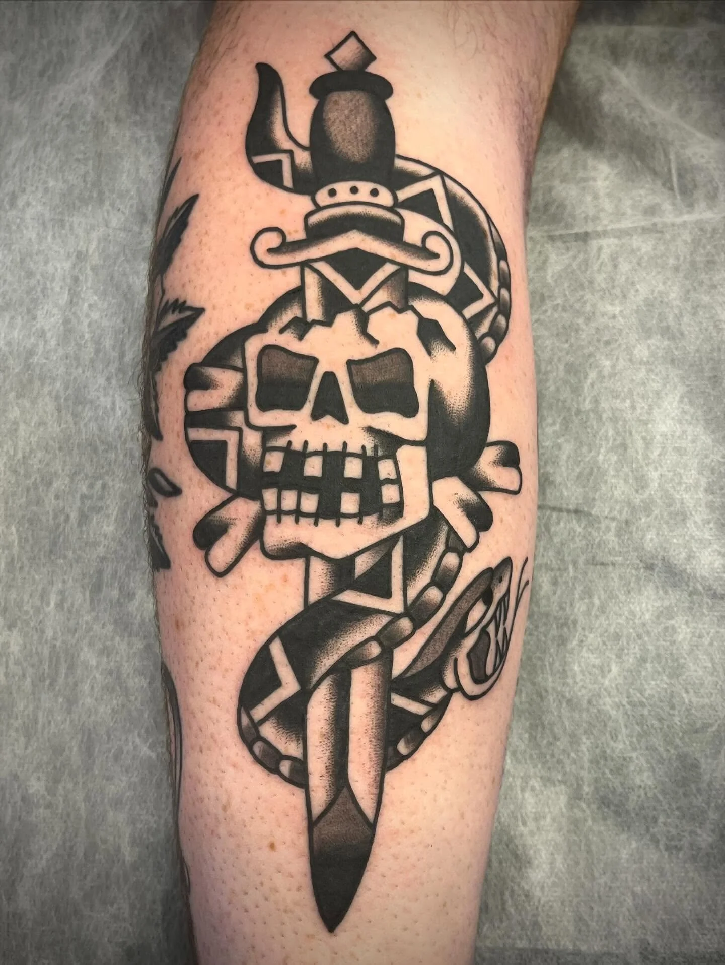 Black and gray tattoo of a pirate skull with a sword piercing through it, surrounded by nautical themes on a person's arm.