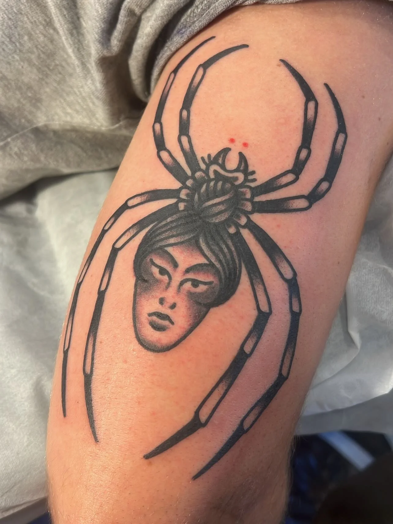Tattoo of a woman’s face with a spider above her head on upper arm.