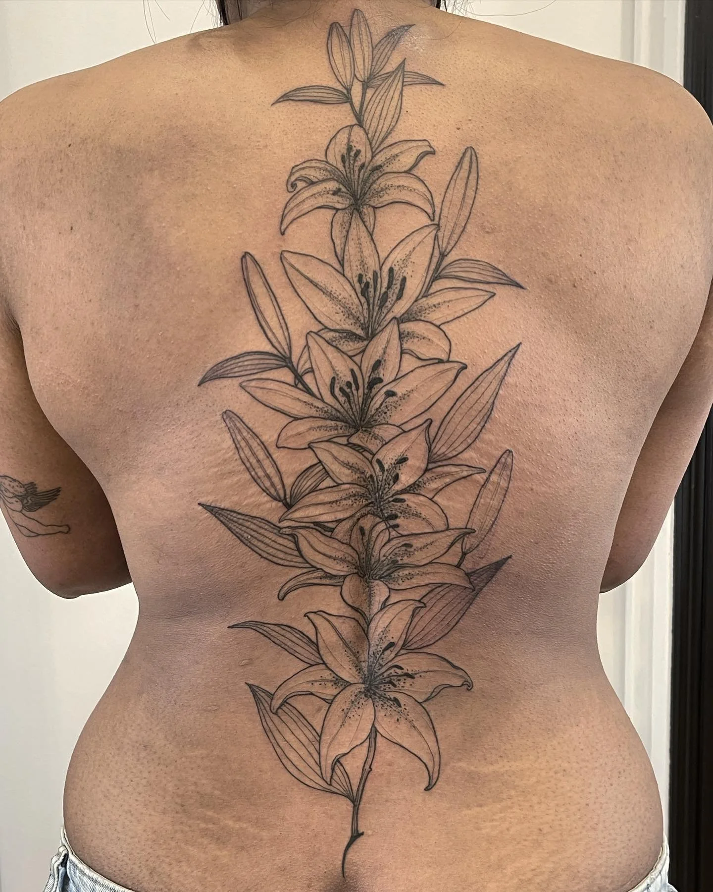 Back tattoo of a vertical row of lily flowers with detailed line work and shading, extending from the upper back to the lower back