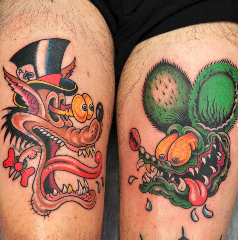 Two cartoon-style tattoo designs on thighs: one features a mischievous, stylized wolf or fox with a top hat, buck teeth, and a playful expression; the other depicts a green creature with large eyes and a long tongue, with sharp teeth and a goofy face
