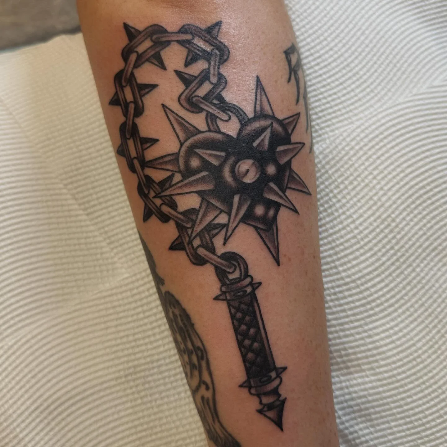 Tattoo of a medieval-style dagger with a spiked mace head, wrapped in a chain, on a person's arm.