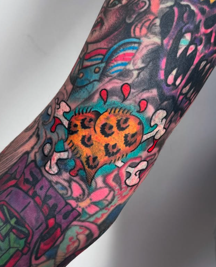 Tattoo of a broken heart with leopard print pattern surrounded by colorful, graffiti-style artwork on arm.