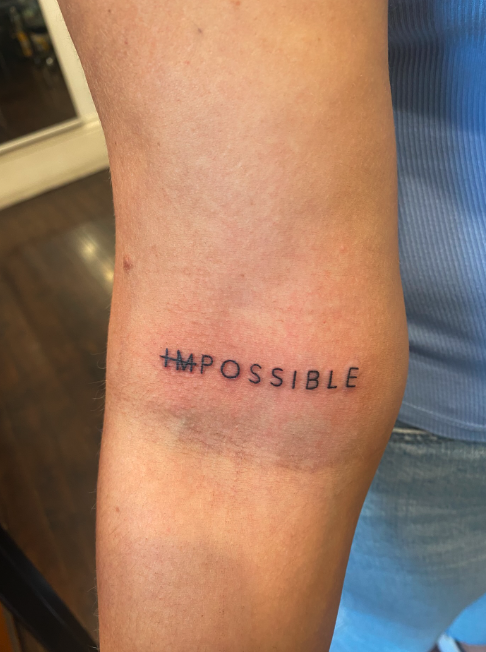 Tattoo on inner arm with the word 'Impossible' crossed out and replaced with 'Possible'.