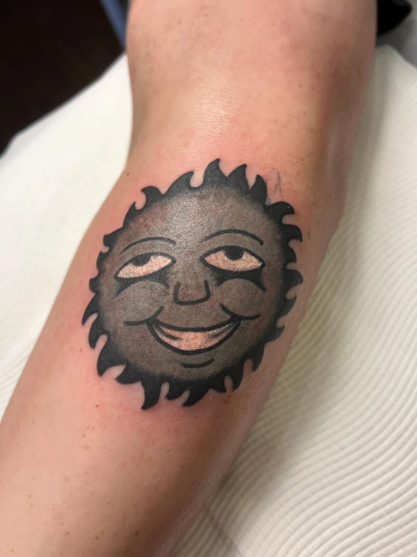 Tattoo of a smiling sun with a human face on a person's arm.
