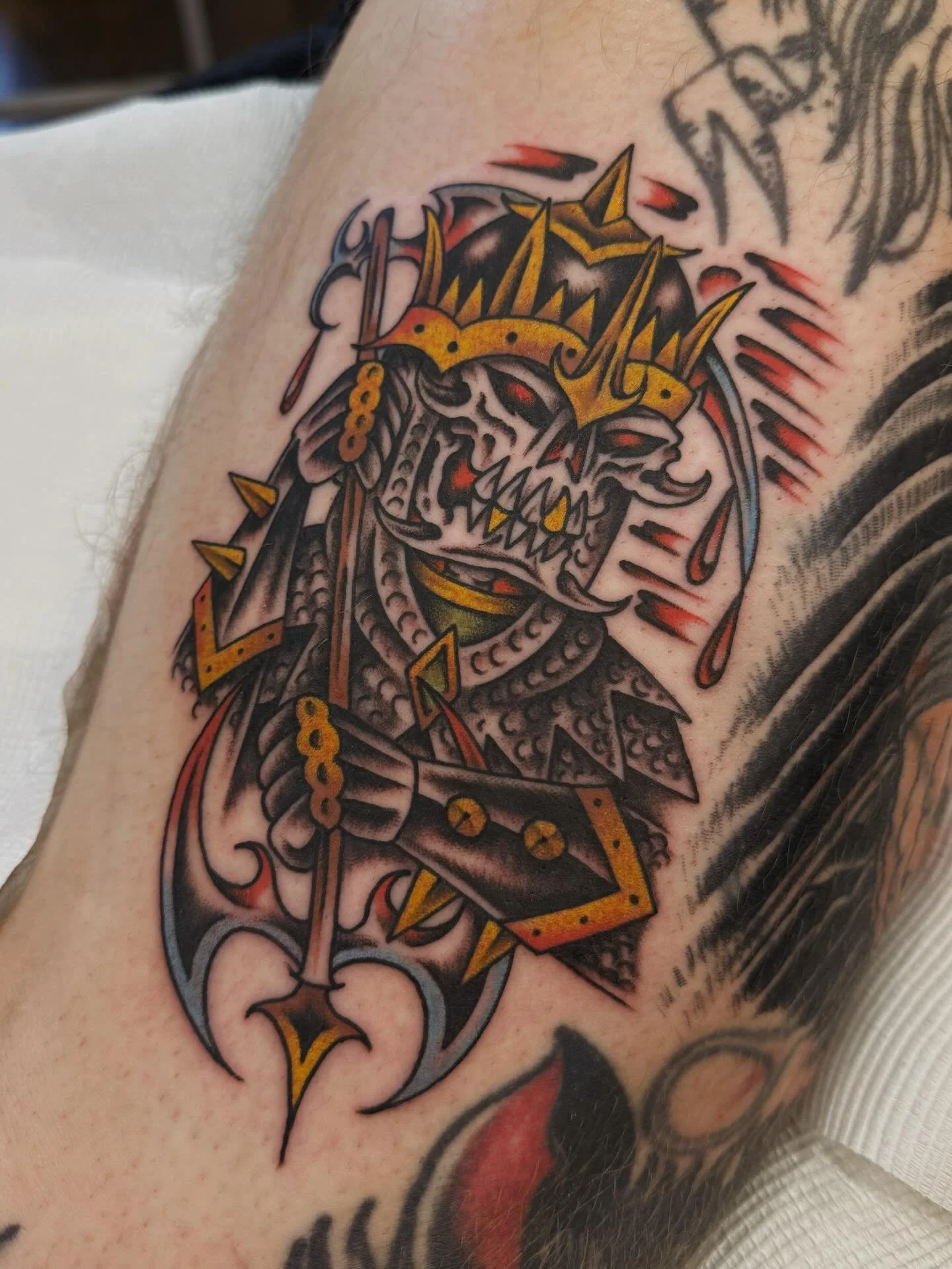 Tattoo of a fierce tiger with a crown and armor, holding an axe, with red accents and dripping blood details.
