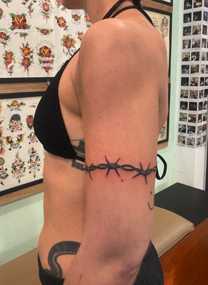 Side view of a woman with tattoos, wearing a black top, in an art studio or tattoo parlor.