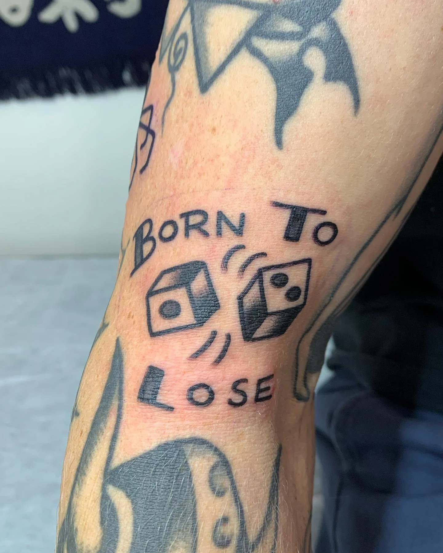 Tattoo on arm that reads 'Born To Lose' with two dice between the words