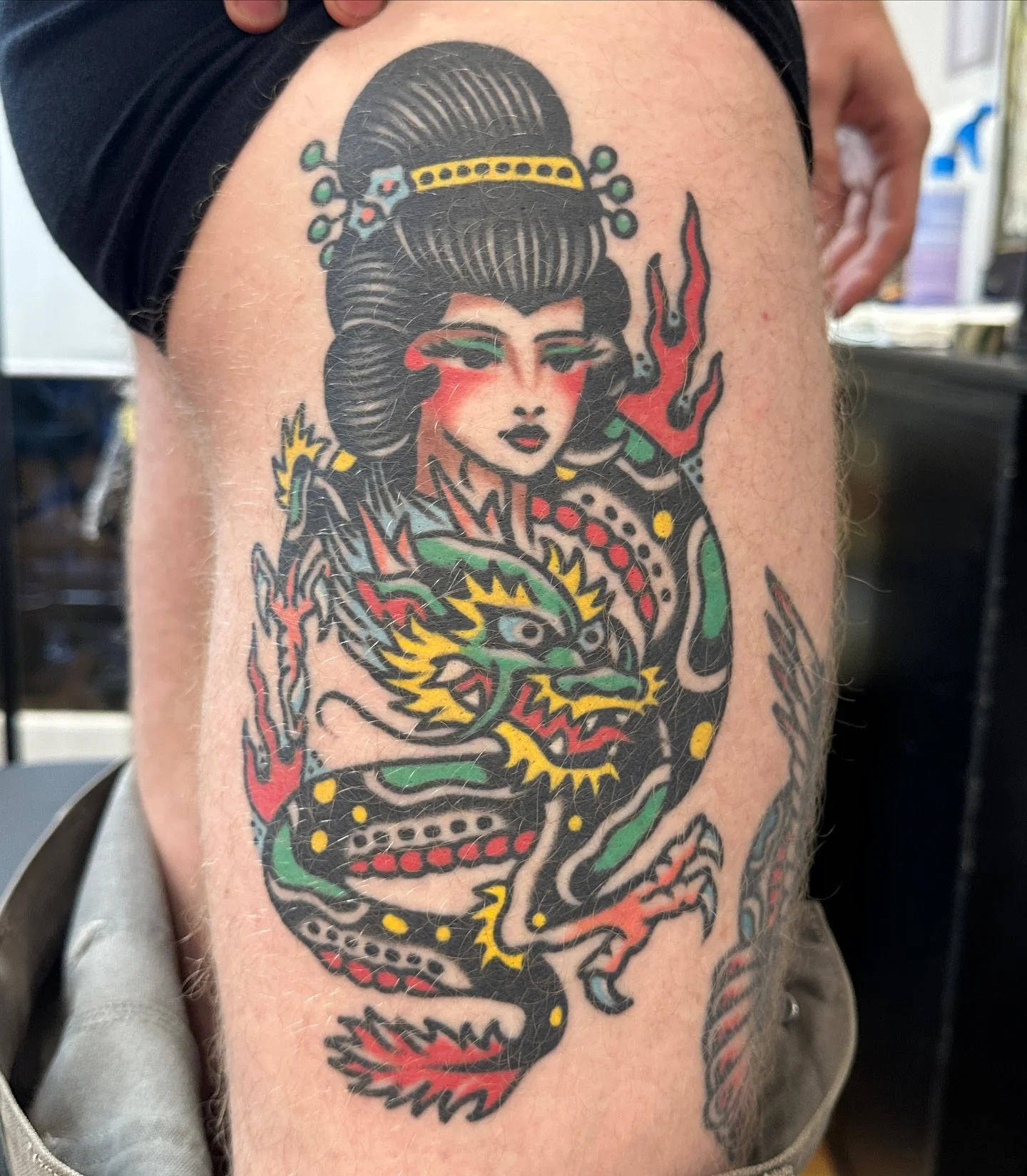 Tattoo of a traditional Japanese-style woman with a dragon, featuring bold black outlines and red, green, yellow accents.
