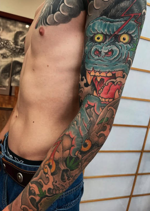 Tattoo of a blue, fierce creature with yellow eyes and an open mouth on person's arm.