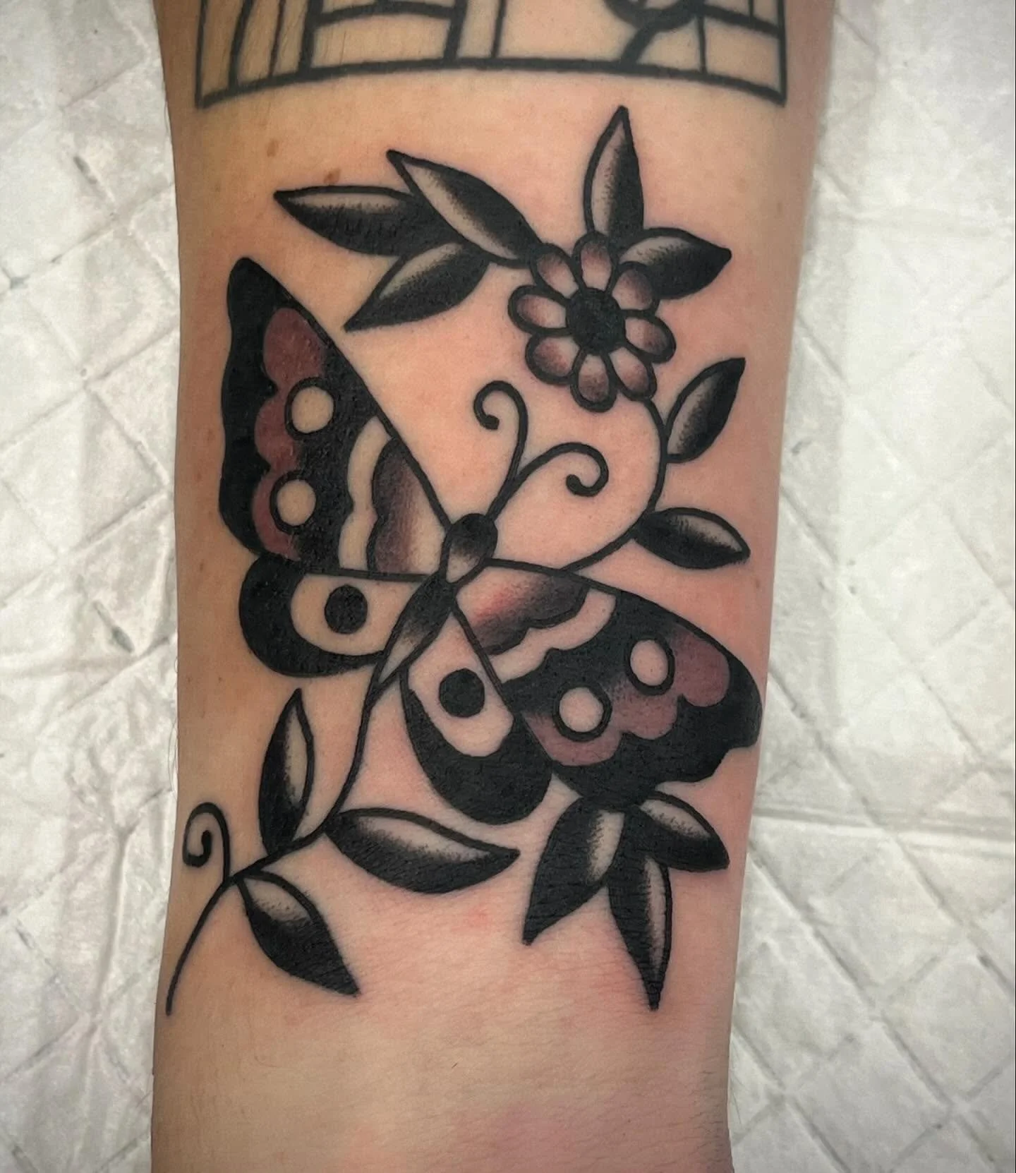 A black and gray tattoo of a butterfly with floral and leaf designs on a person's arm.