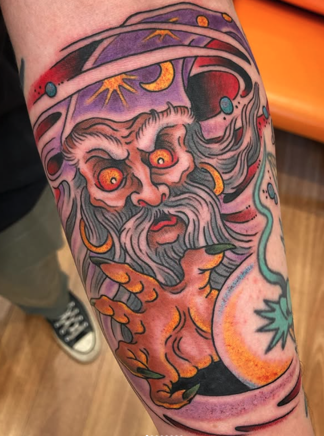 Tattoo of a wizard with orange eyes, long gray beard, and pointed fingers casting a spell in space with planets and celestial bodies.