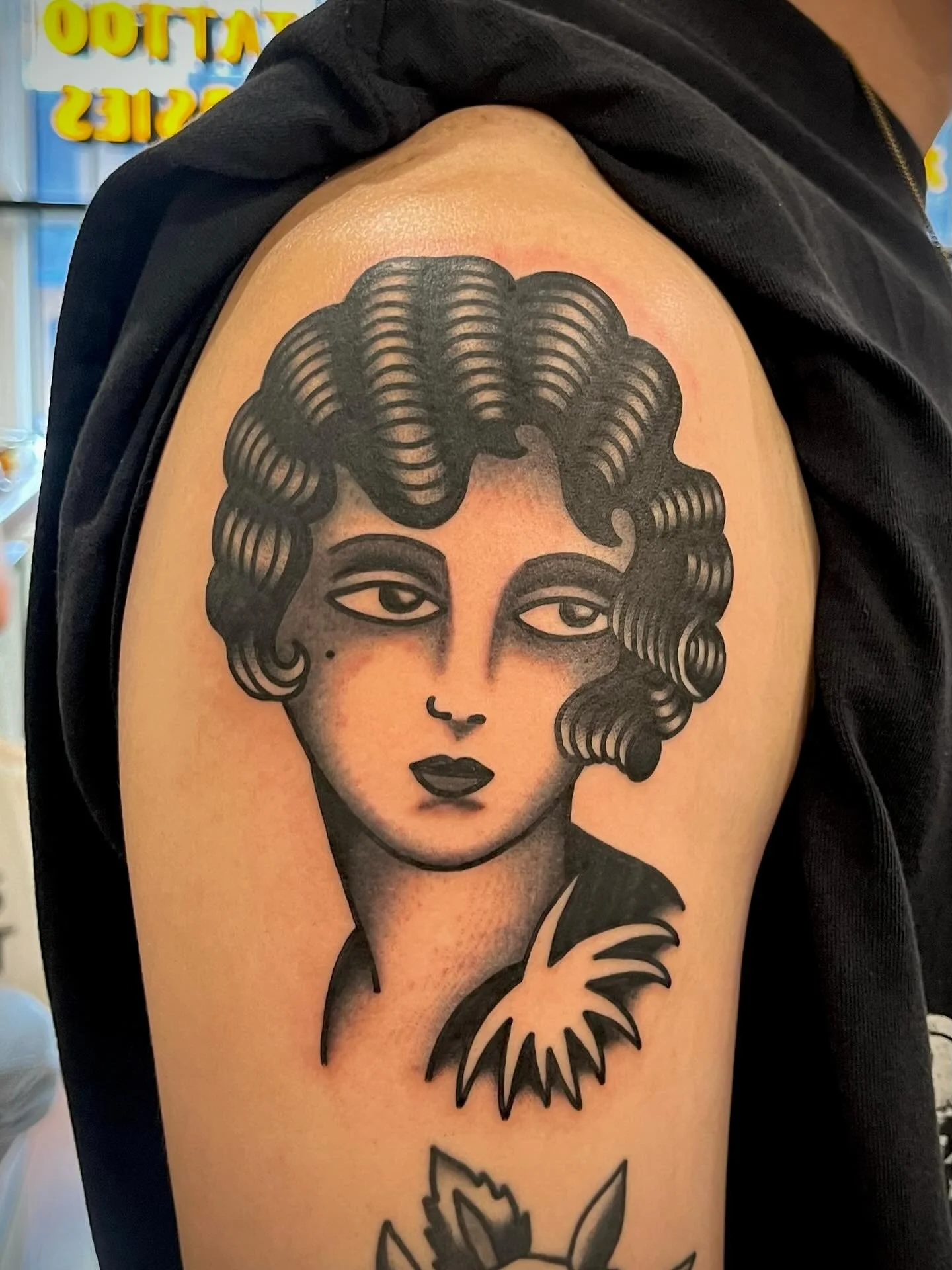 Tattoo of a woman's face with curly hair, dark lipstick, and expressive eyes, on upper arm.