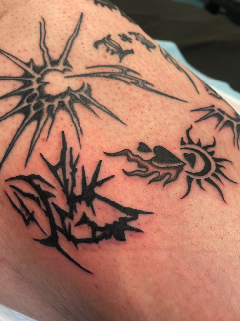 Close-up of a tattoo on skin featuring a sun, a moon with flames, a cloud, and stylized text.