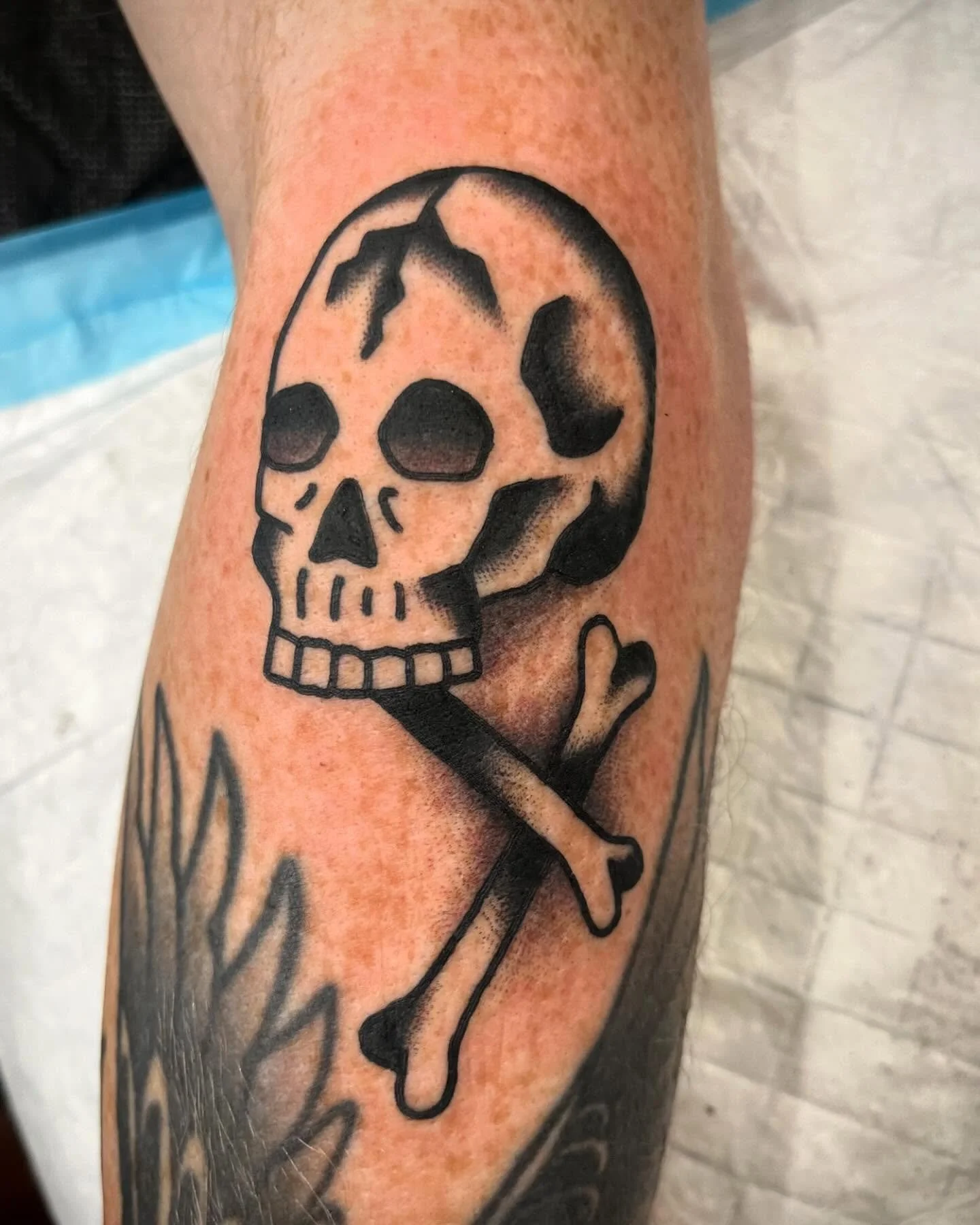 Tattoo of a skull with a crossed bone underneath.