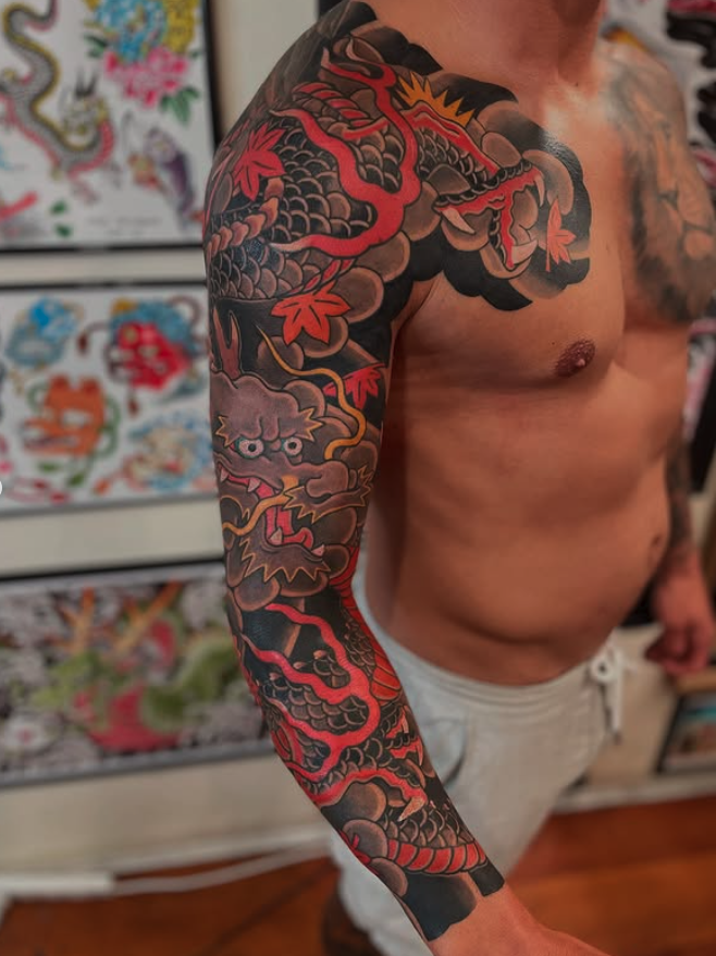 A man with a black and red Japanese-style dragon tattoo covering his left arm and shoulder.