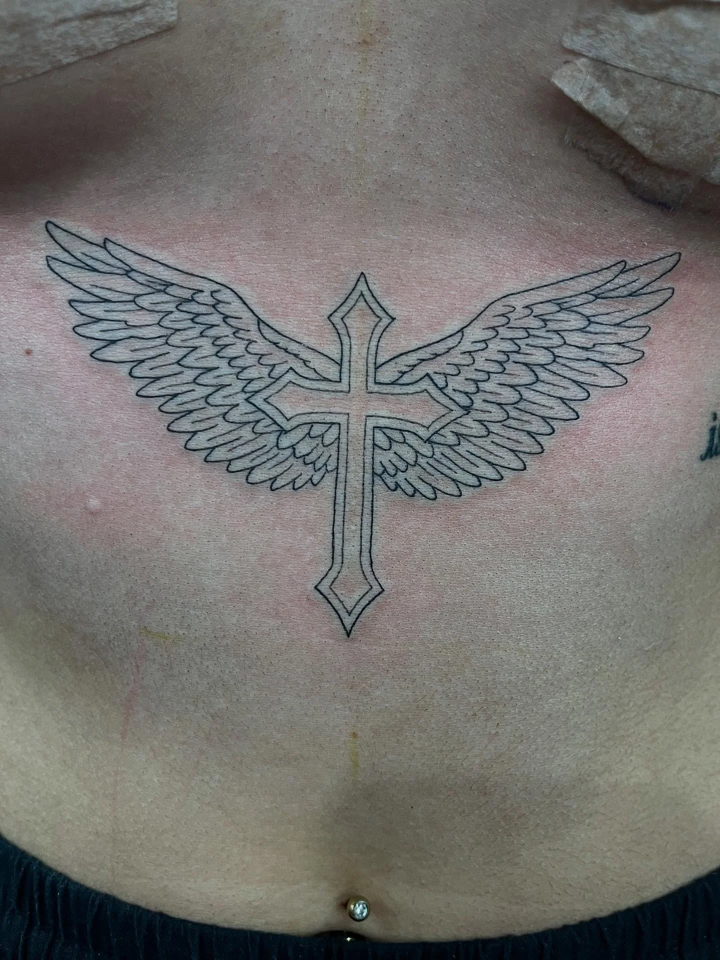 Tattoo of a cross with angel wings on a person's chest.