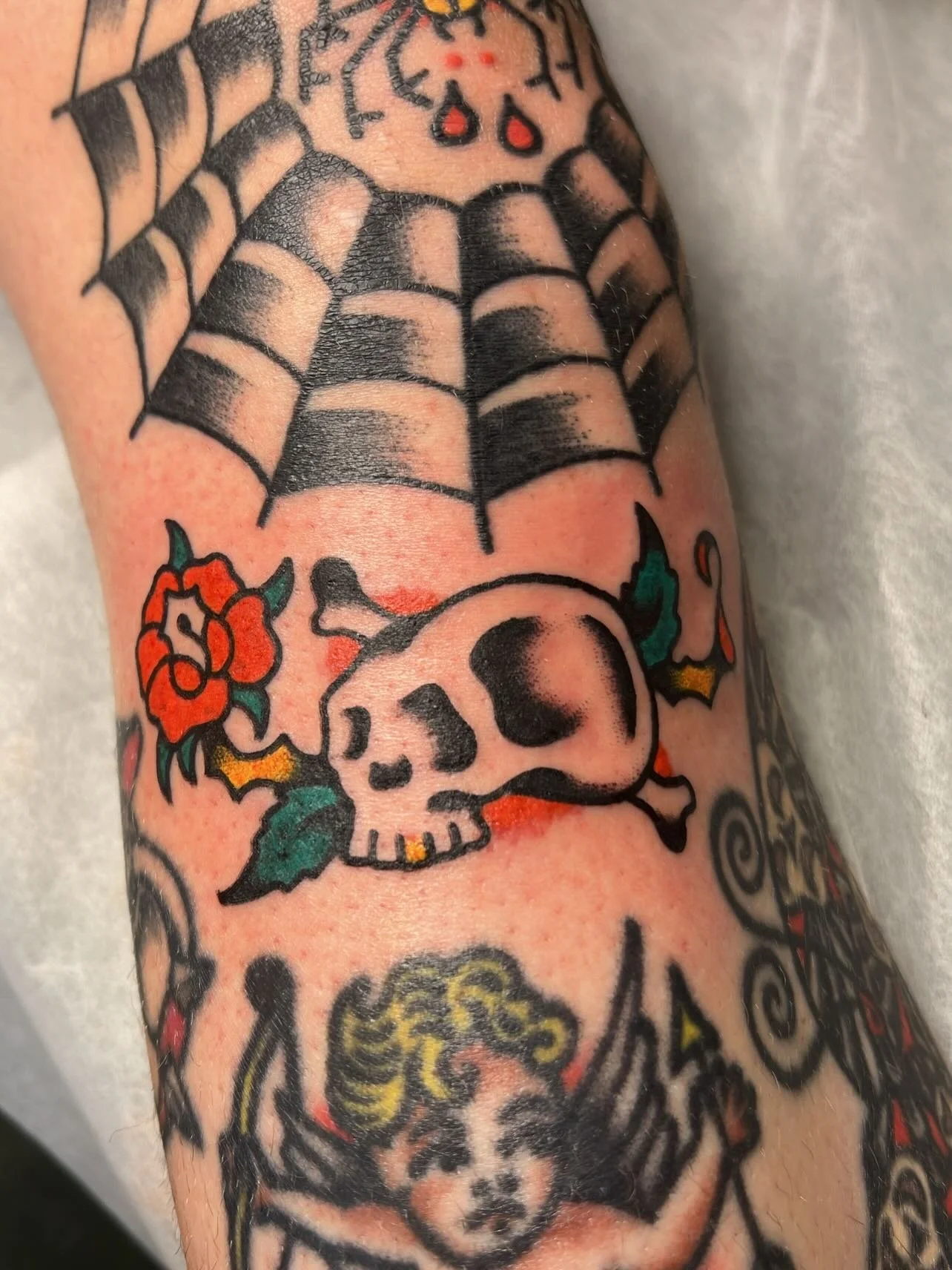 Tattoo of a spider web above a skull with roses and other designs on skin.