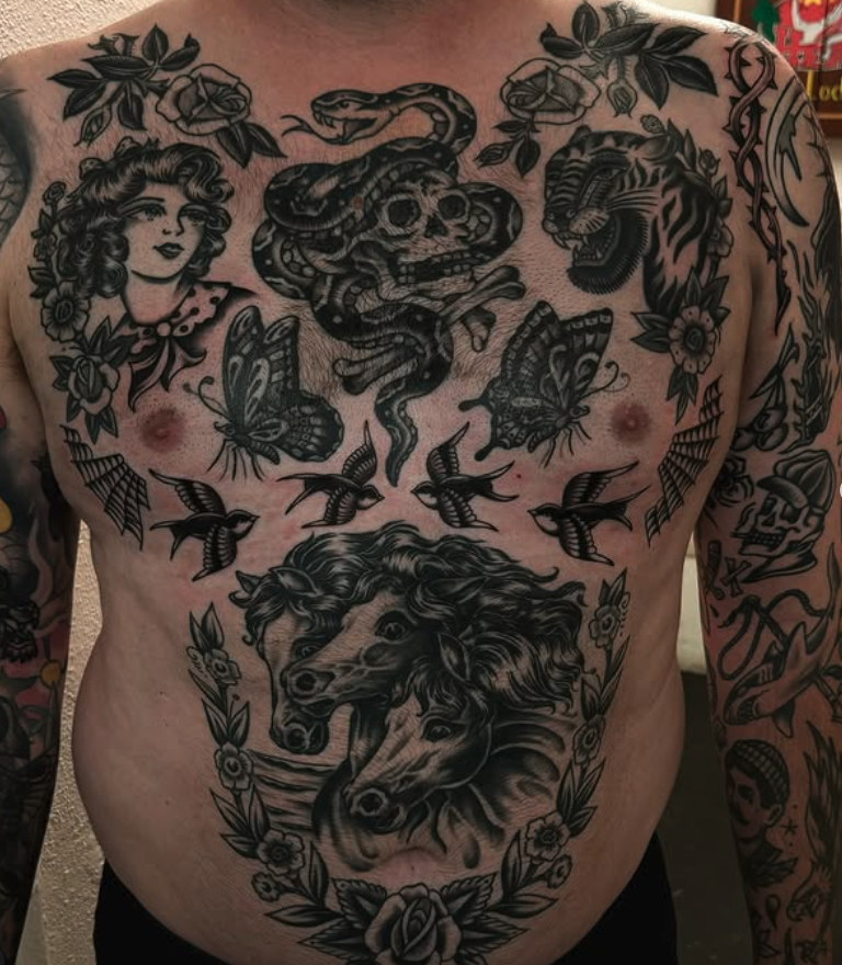 Tattooed man with black and gray tattoos on chest and arms, featuring a snake, a skull, a lion, a butterfly, a woman, birds, flowers, and various other designs.
