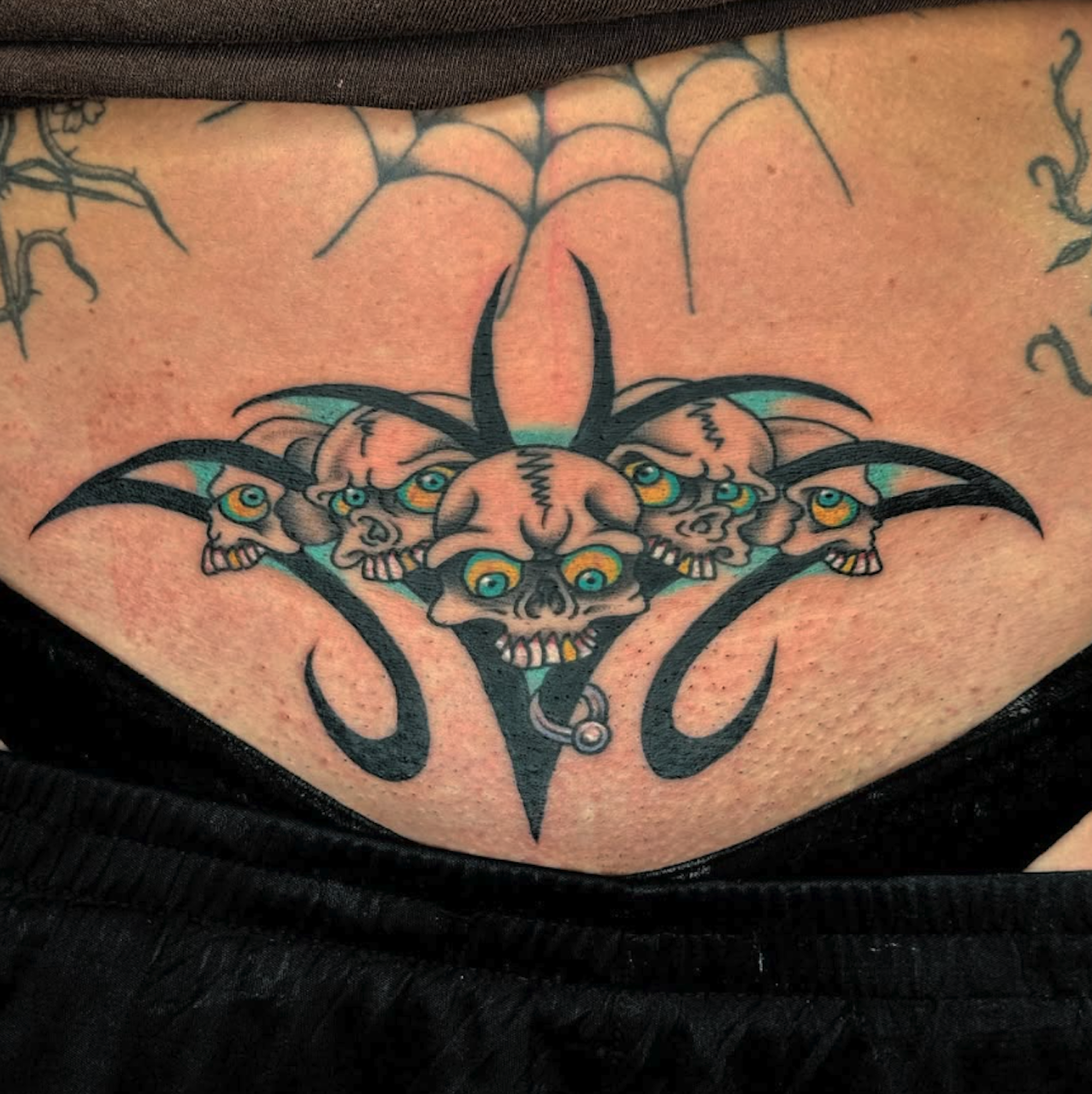 Tattoo of a bat with multiple bat skulls with yellow eyes on a person's chest.
