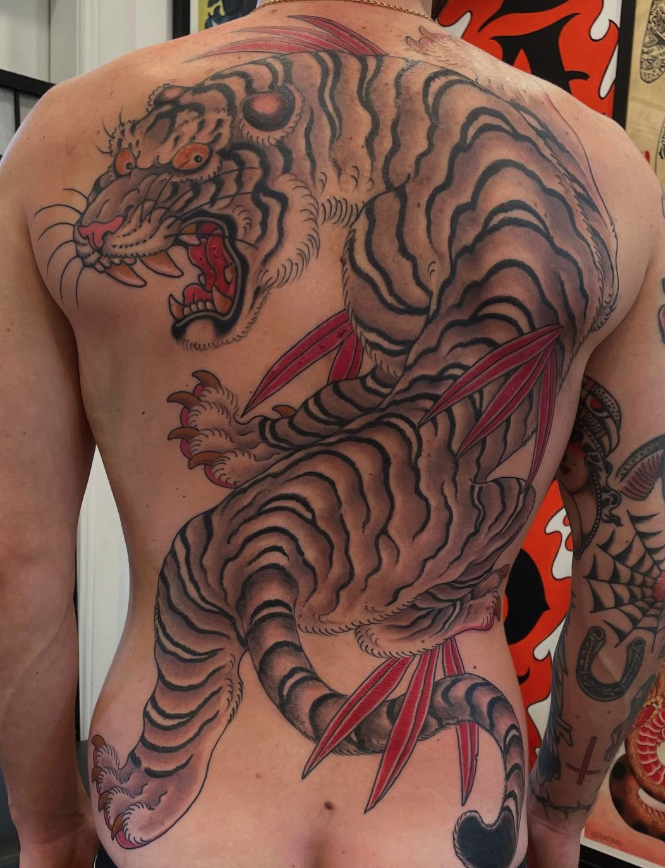 Tattoo of a large, aggressive tiger with sharp claws and open mouth, covered in black and orange stripes, on a person's chest and side.