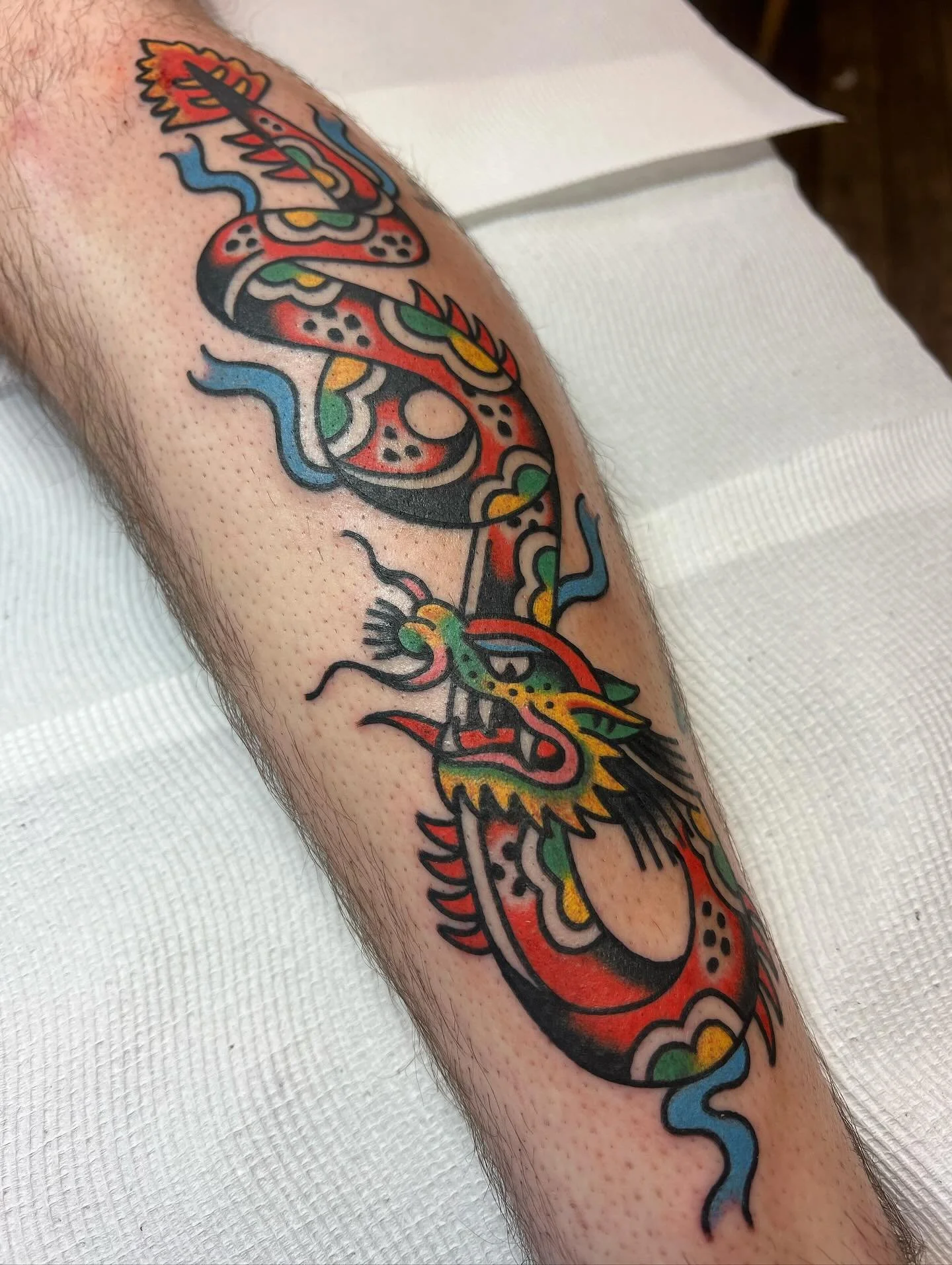Colorful Japanese-style dragon tattoo on a person's forearm, featuring bold black outlines, red, yellow, green, and blue accents, and intricate detailing.