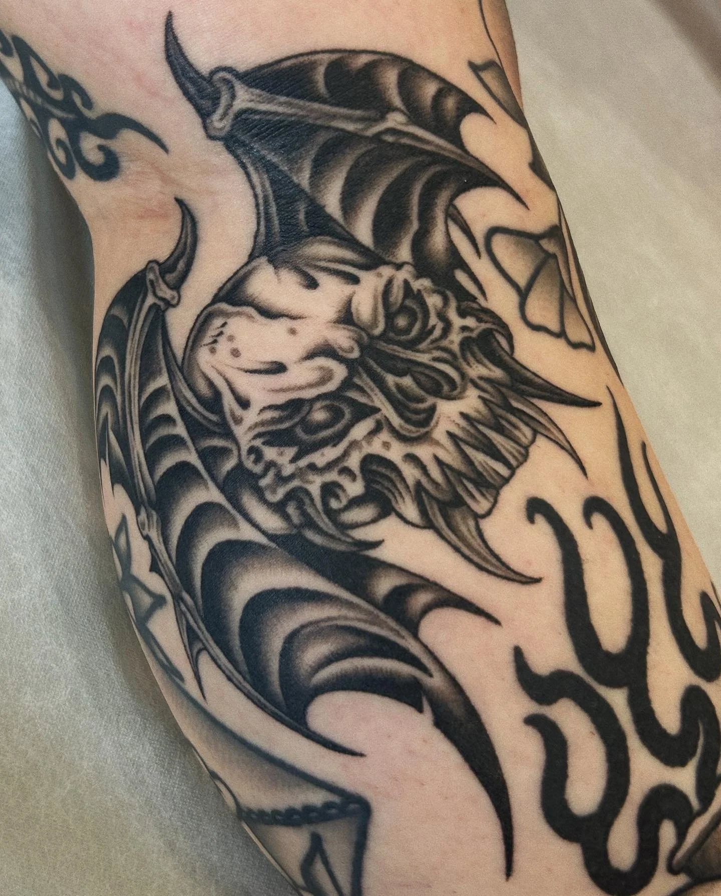 Black and gray tattoo of a fierce dragon's head with large wings on a person's arm.