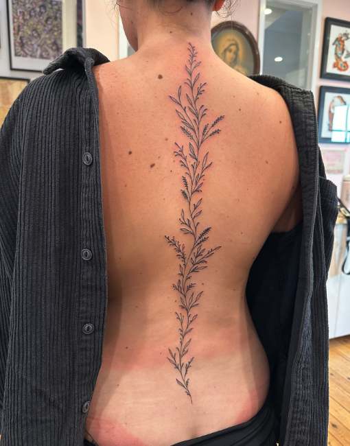 A woman with a long, vertical tattoo resembling a leafy vine running down her back from her neck to her lower back.