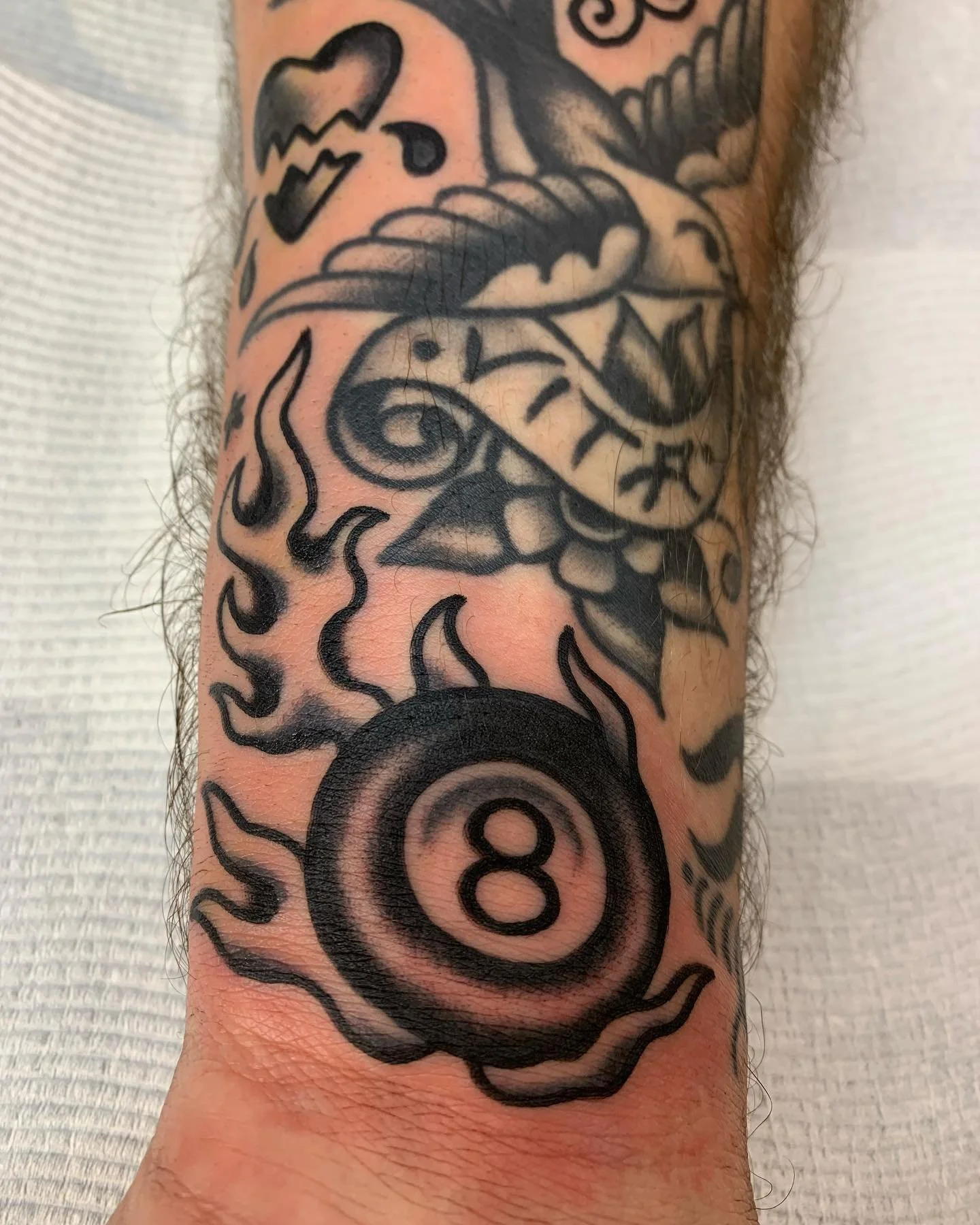 Tattoo of a flaming 8-ball, a dagger with a rose, and a small skull on a person's arm.