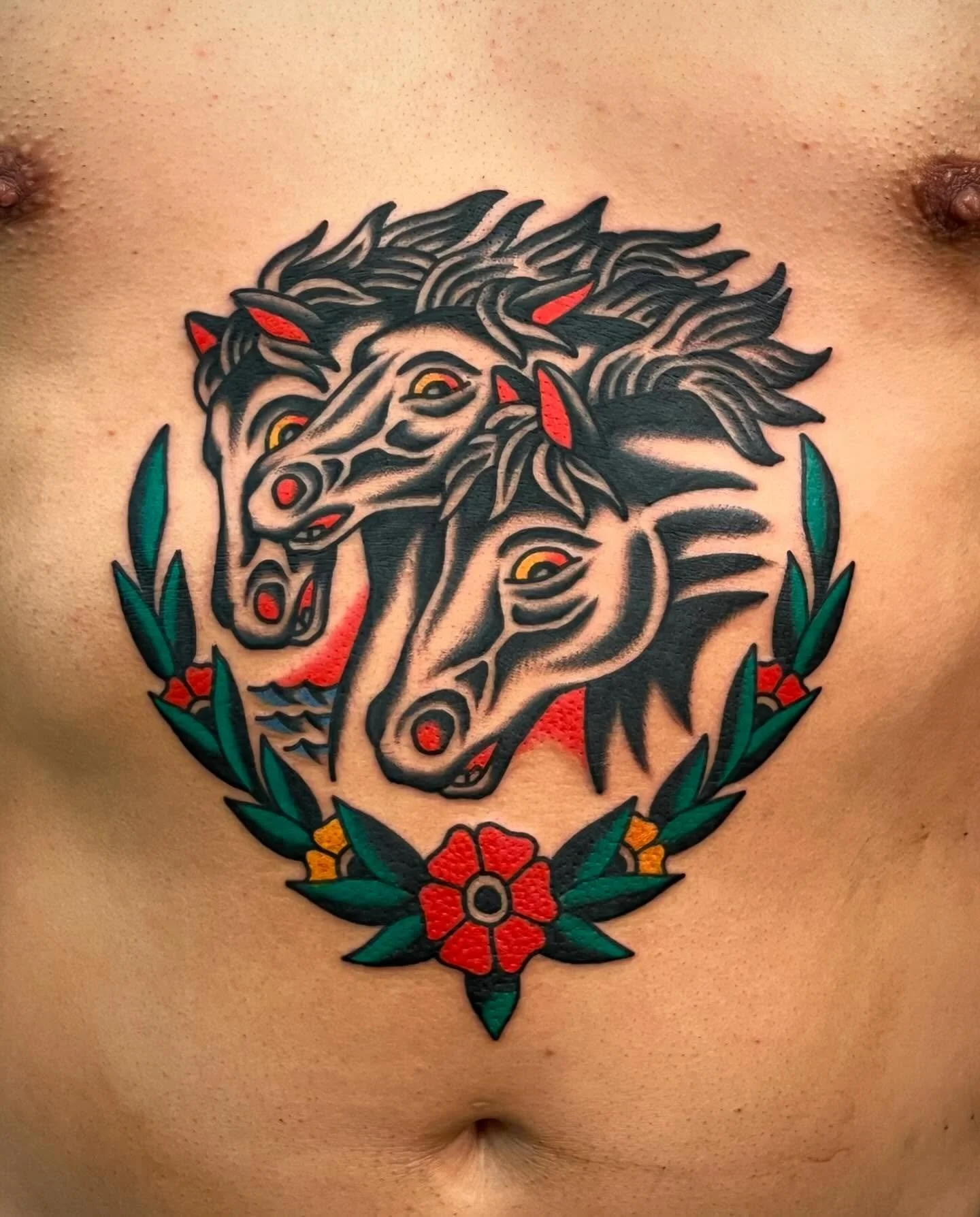 Tattoo of three stylized wolves with open mouths, surrounded by green leaves and red flowers on a person's chest.
