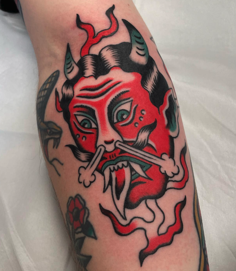 A tattoo of a traditional Japanese demon mask with horns, sharp teeth, and red and black details.