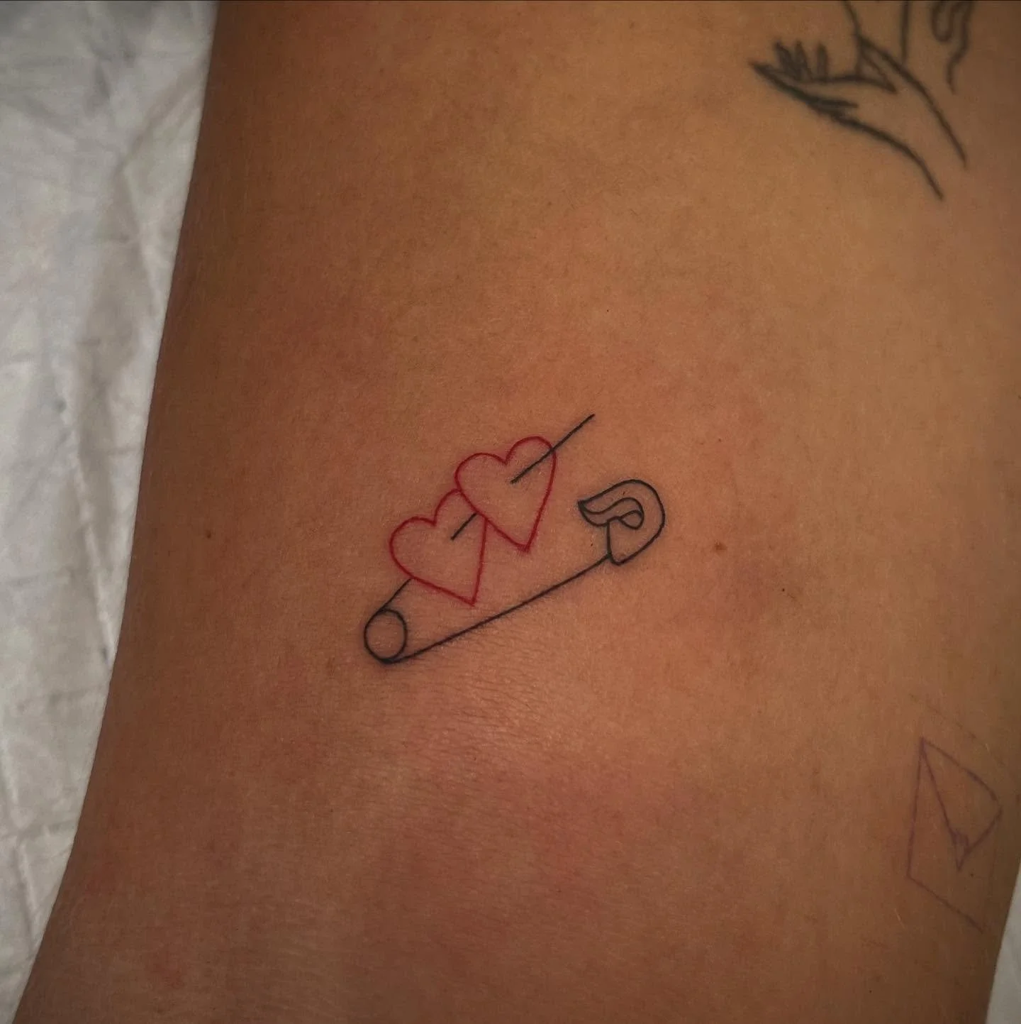 Tattoo of two red hearts pierced by a black arrow, laid on a black arrow with a small curved line at one end, on skin.