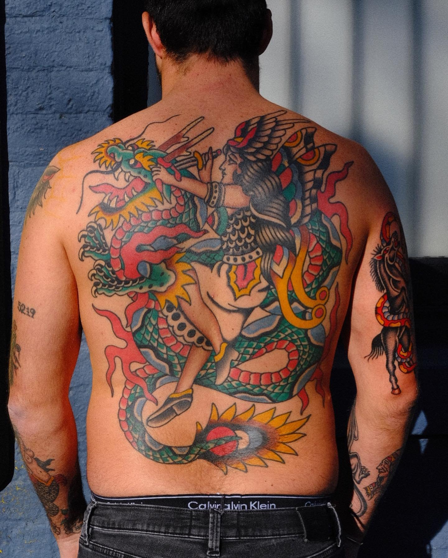 Back tattoo of a warrior character battling a dragon with colorful flames and scales.