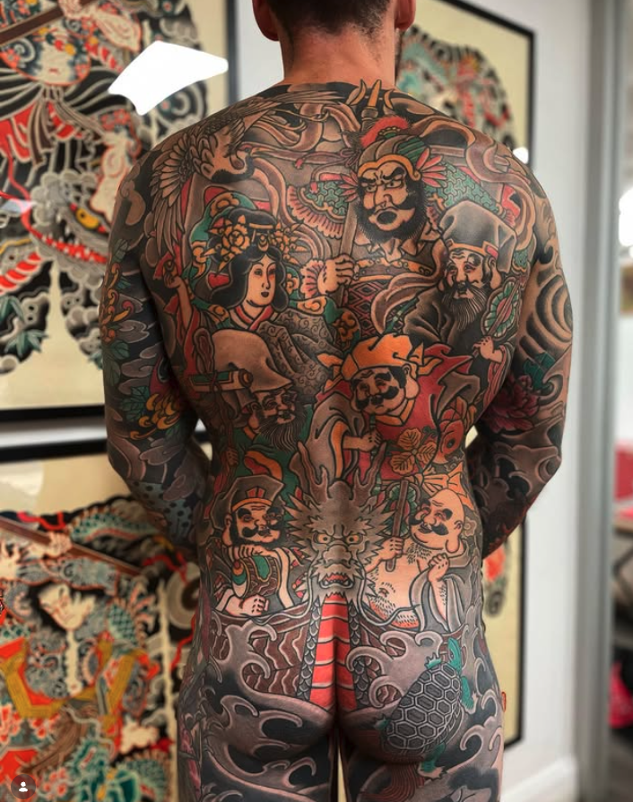 A man with a large, colorful full-back tattoo featuring traditional Japanese-style warrior and mythological figures, dragons, and clouds.