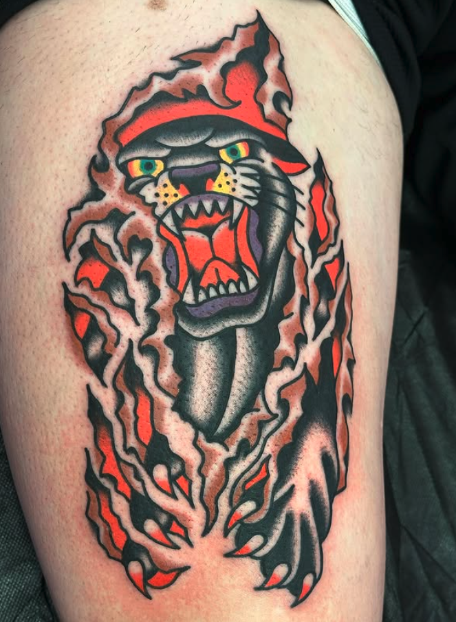 Tattoo of a roaring tiger with green eyes, open mouth showing teeth, surrounded by flames in black, orange, and purple on skin.