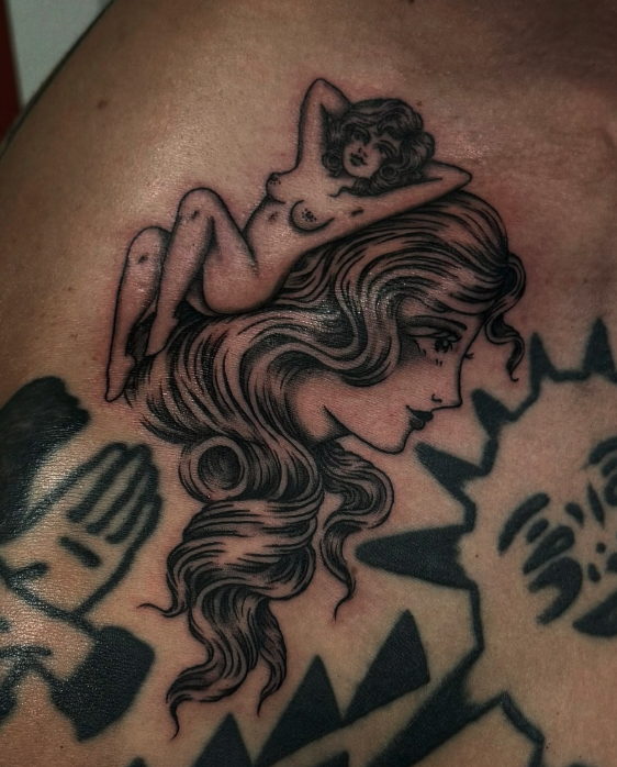 Tattoo of a woman with flowing hair and a small reclining nude woman on her head.
