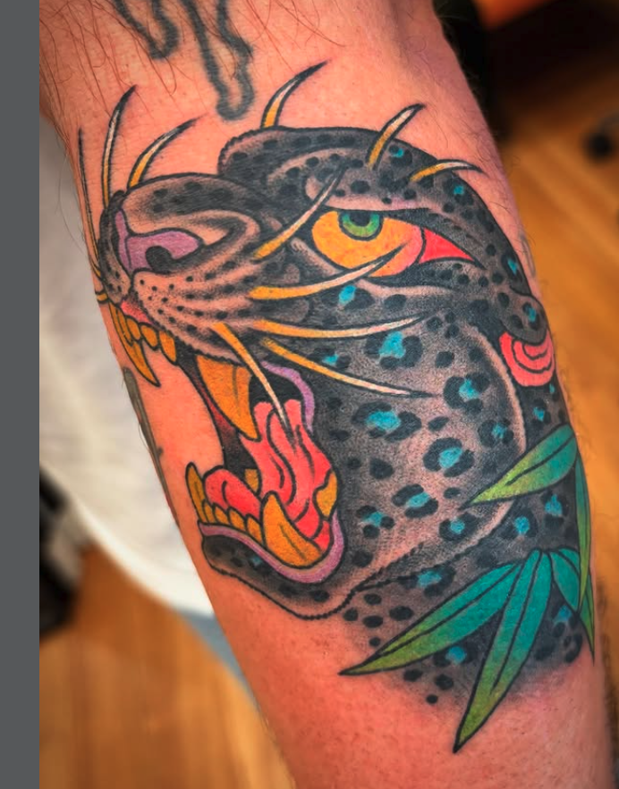 Tattoo of a roaring leopard with colorful details, includes green leaves.