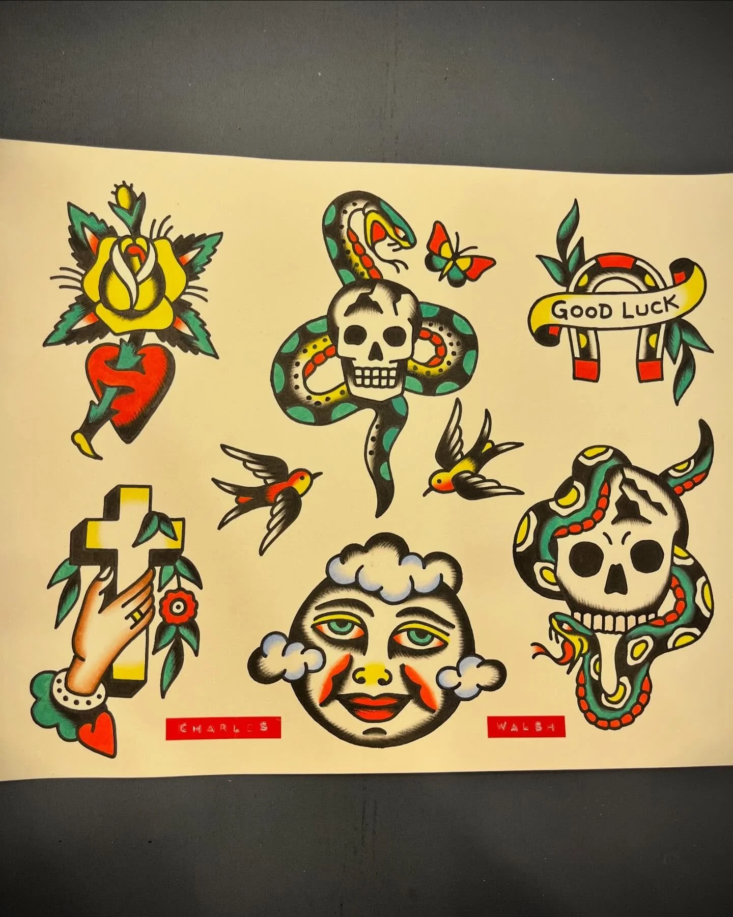 Collection of traditional tattoo-style illustrations including a yellow rose with a dagger, a snake with a skull, a 'Good Luck' horseshoe, a hand holding a cross with a flower, a smiling woman's face with clouds, two hummingbirds, and a skull with sn