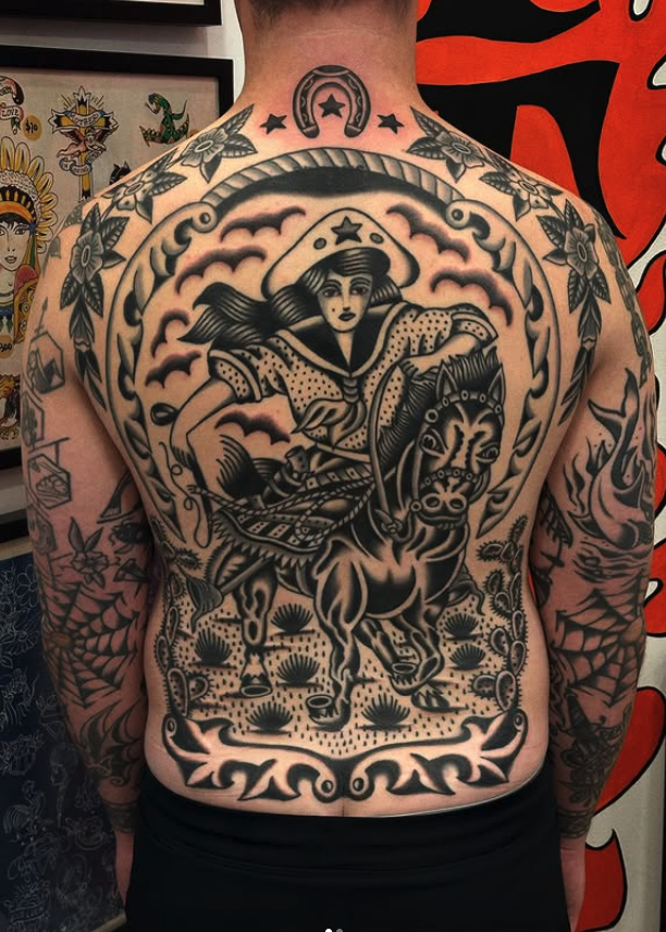 A person with a large chest tattoo featuring a woman in a hat riding a horse, surrounded by clouds and decorative borders in black ink.