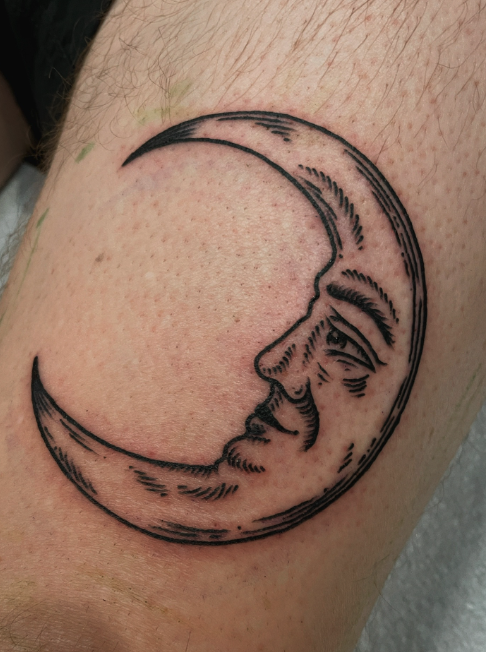 Tattoo of a crescent moon with a human face on skin.