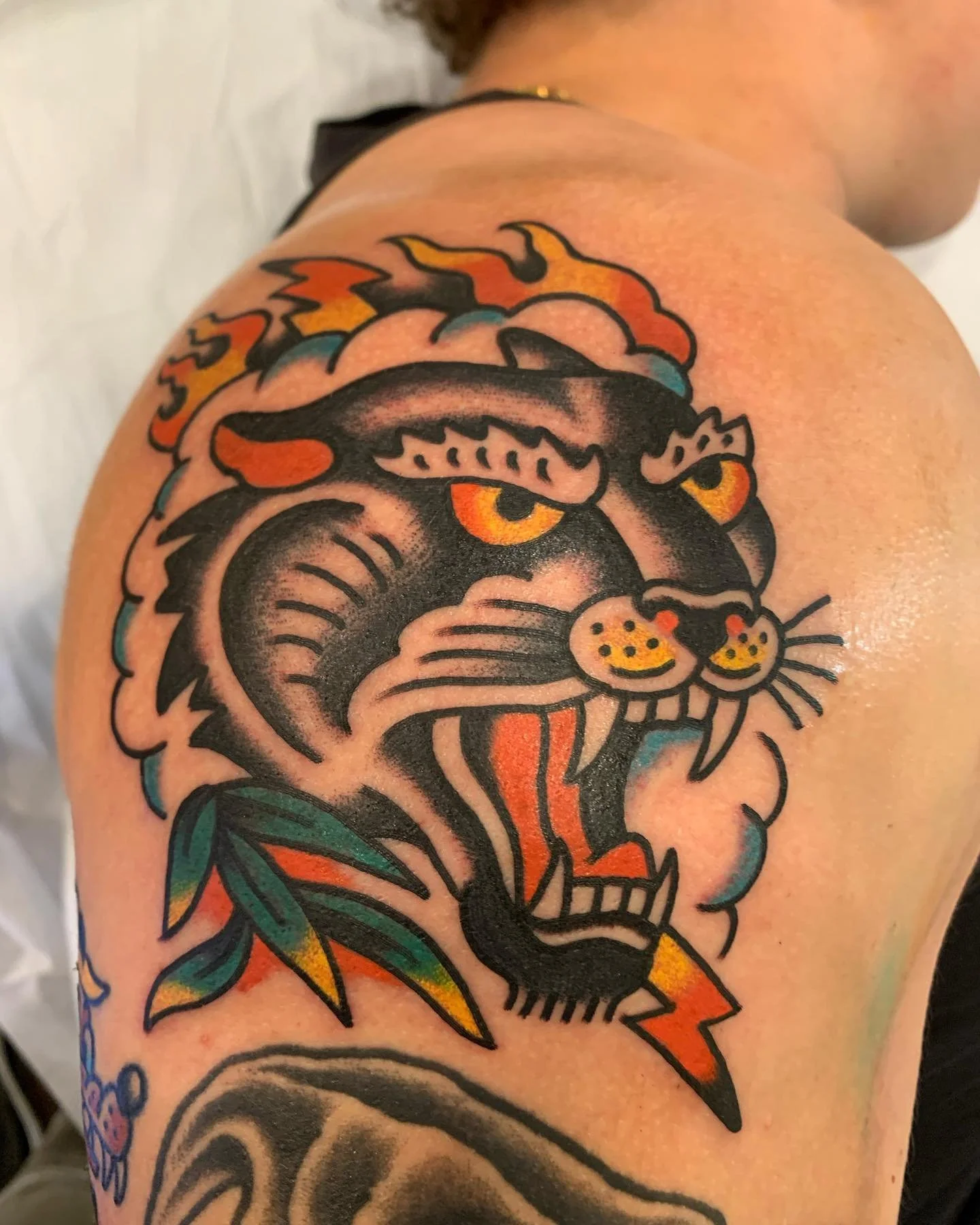Tattoo of a fierce tiger's face with yellow eyes and an open mouth, surrounded by flames and lightning, in traditional style with black outlines and bright colors.