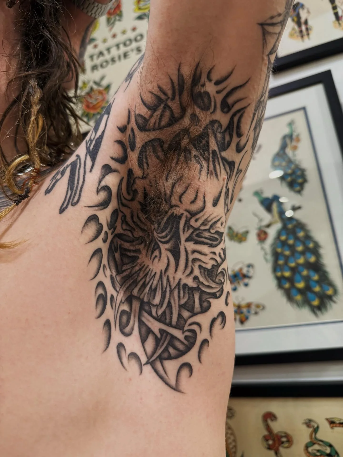 Black and gray tattoo of a fierce tiger's face on a person's upper arm, with stylized surrounding flames or tribal design elements.