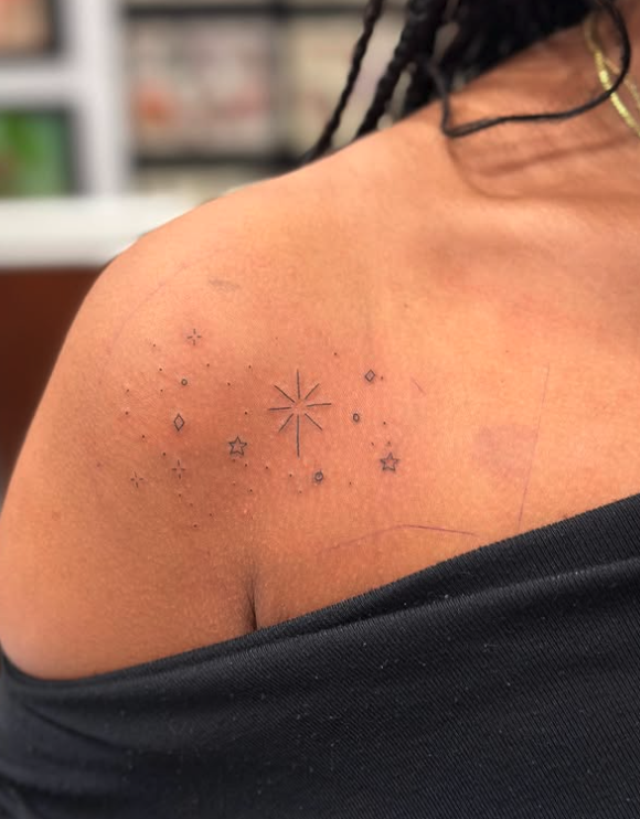 Tattoo of small stars and a central radiant starburst on woman's shoulder.