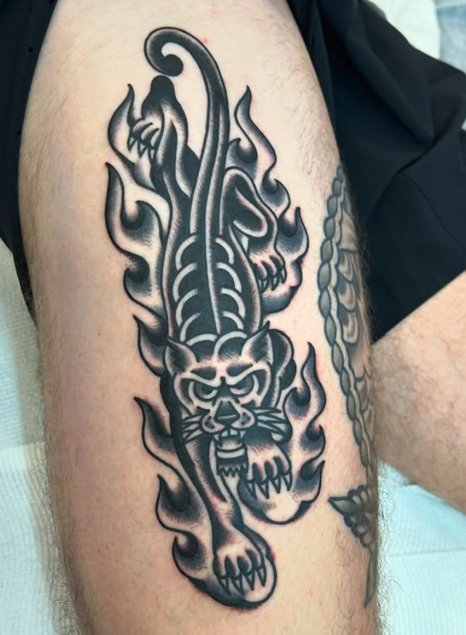 Black and gray tattoo of a fierce tiger with flames and stylized elements on a person's thigh.