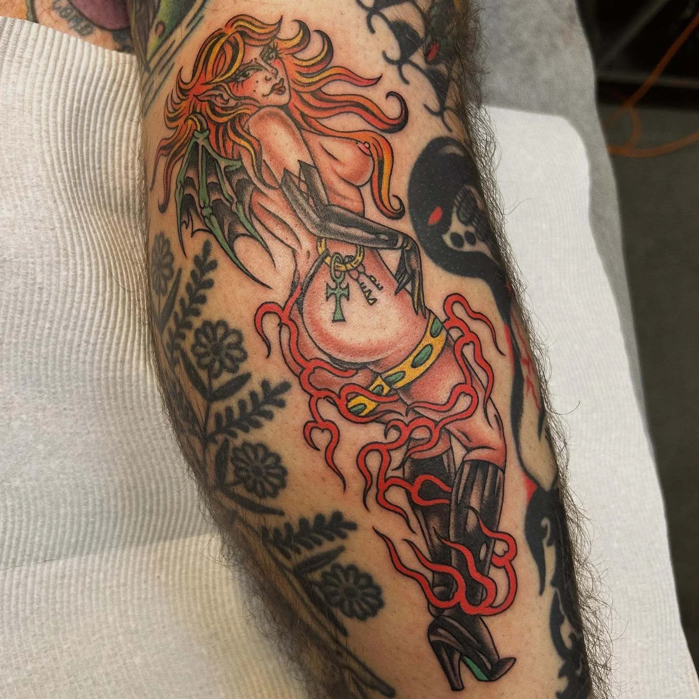 Tattoo of a fantasy female figure with wings, holding a sword, surrounded by red tentacle-like shapes and floral patterns on an arm.