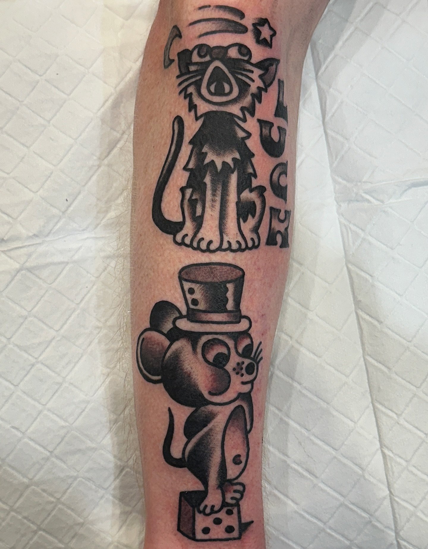 Tattoo of a cartoonish dog with glasses and a star, labeled 'RESCUE,' above a mouse with a top hat, standing on a piece of cheese.